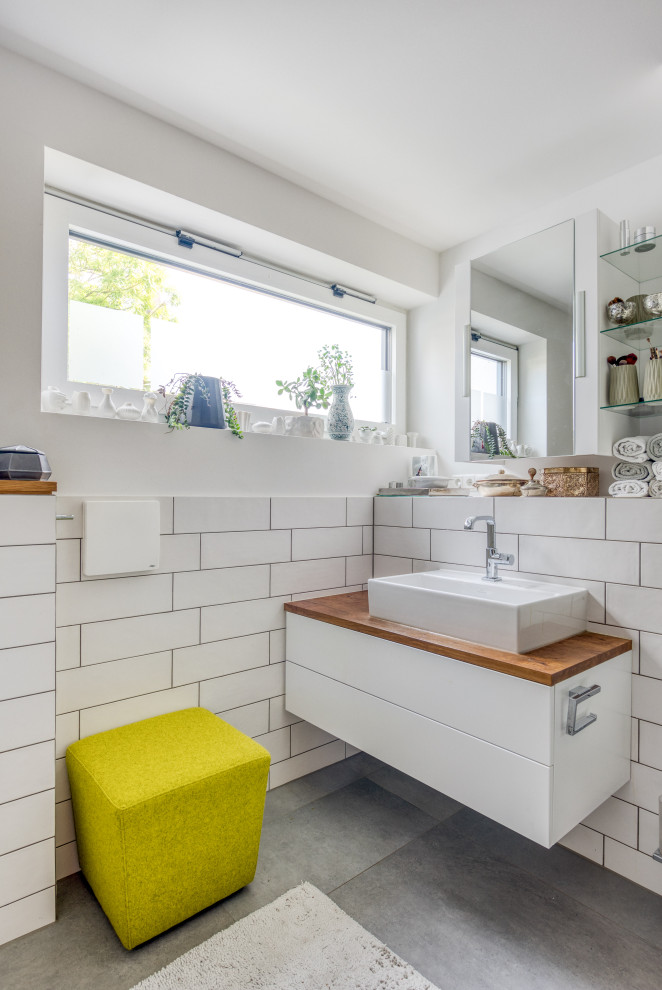 Kleines Modernes Badezimmer mit flächenbündigen Schrankfronten, weißen Schränken, weißen Fliesen, weißer Wandfarbe, Aufsatzwaschbecken, Waschtisch aus Holz, grauem Boden, brauner Waschtischplatte, Einzelwaschbecken und schwebendem Waschtisch in München