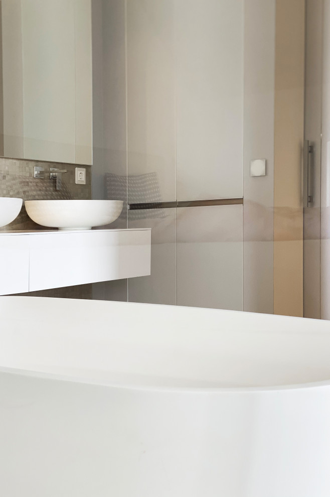 This is an example of an expansive contemporary ensuite bathroom in Other with flat-panel cabinets, grey cabinets, a freestanding bath, a walk-in shower, a wall mounted toilet, grey tiles, mosaic tiles, grey walls, ceramic flooring, a vessel sink, solid surface worktops, white floors, an open shower, white worktops, a wall niche, double sinks and a freestanding vanity unit.