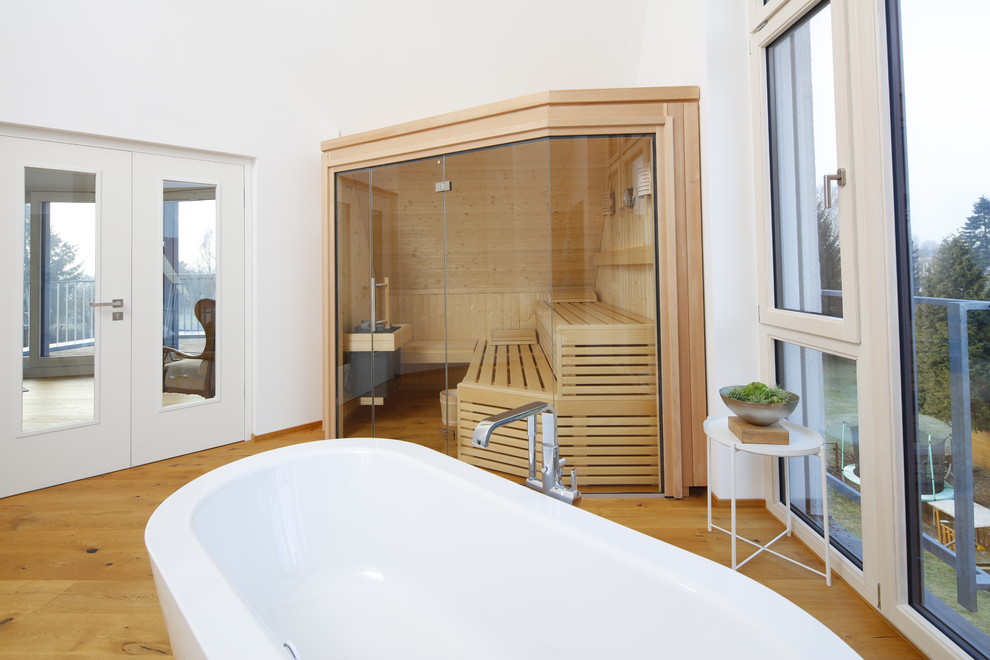 Ispirazione per una sauna nordica di medie dimensioni con vasca freestanding, pareti bianche, pavimento in legno massello medio e pavimento marrone