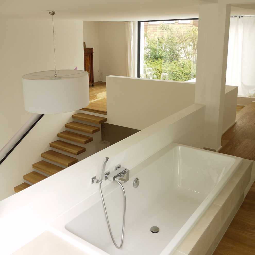 Foto de cuarto de baño actual de tamaño medio con bañera encastrada, paredes blancas, baldosas y/o azulejos beige y suelo de madera en tonos medios