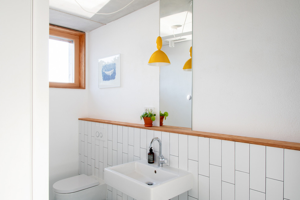 Minimalistisk inredning av ett litet badrum för barn, med en vägghängd toalettstol, vit kakel, vita väggar, ett väggmonterat handfat, en kantlös dusch, keramikplattor, klinkergolv i keramik, bänkskiva i akrylsten, grönt golv och med dusch som är öppen
