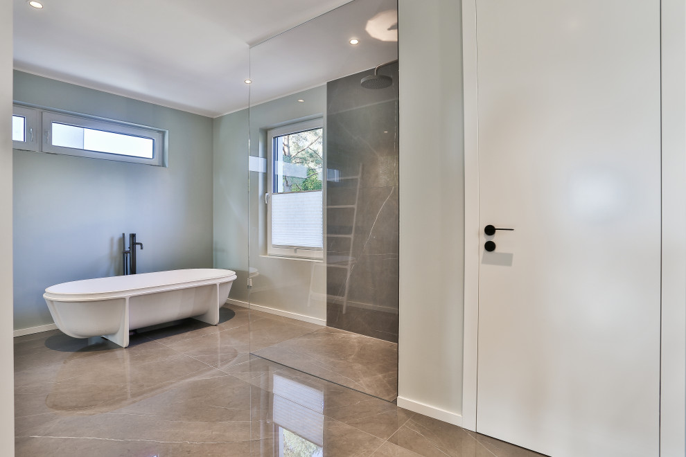 Bild på ett mellanstort funkis grå grått en-suite badrum, med grå skåp, ett fristående badkar, en kantlös dusch, en vägghängd toalettstol, grå kakel, marmorkakel, gröna väggar, marmorgolv, ett integrerad handfat, bänkskiva i glas, grått golv och med dusch som är öppen