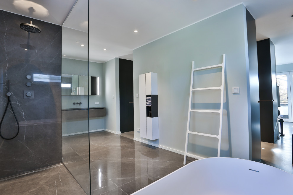 Bild på ett mellanstort funkis grå grått en-suite badrum, med grå skåp, ett fristående badkar, en kantlös dusch, en vägghängd toalettstol, grå kakel, marmorkakel, gröna väggar, marmorgolv, ett integrerad handfat, bänkskiva i glas, grått golv och med dusch som är öppen