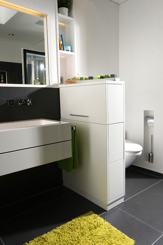 This is an example of a small contemporary bathroom in Other with flat-panel cabinets, white cabinets, grey tiles, cement tiles, white walls, cement flooring, a trough sink, solid surface worktops and brown floors.
