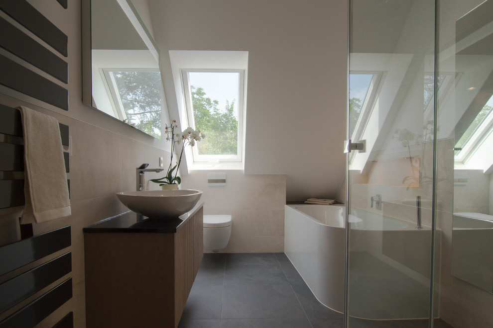 Свежая идея для дизайна: ванная комната среднего размера в современном стиле с плоскими фасадами, светлыми деревянными фасадами, отдельно стоящей ванной, раздельным унитазом, бежевой плиткой, белыми стенами, душевой кабиной, настольной раковиной, серым полом, душем с распашными дверями и черной столешницей - отличное фото интерьера