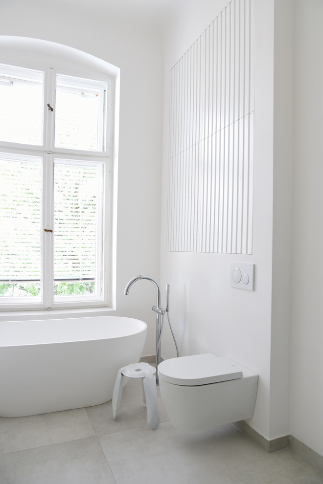 Idéer för ett mellanstort modernt vit en-suite badrum, med luckor med profilerade fronter, vita skåp, ett fristående badkar, en kantlös dusch, en toalettstol med separat cisternkåpa, grå kakel, keramikplattor, vita väggar, ett väggmonterat handfat, bänkskiva i akrylsten och dusch med gångjärnsdörr