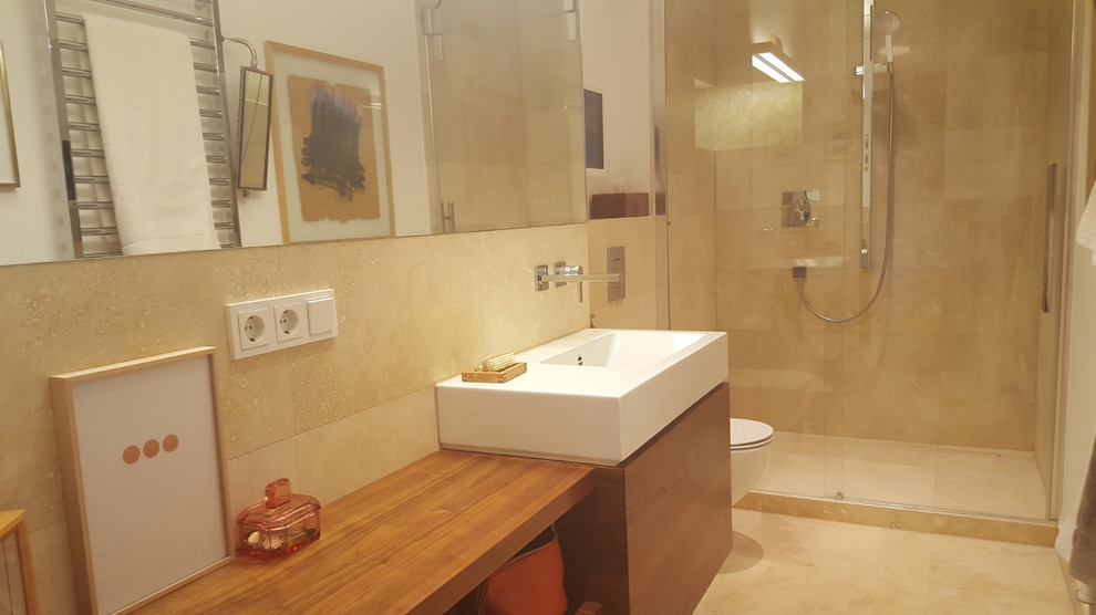 Inspiration for a contemporary shower room bathroom in Berlin with flat-panel cabinets, dark wood cabinets, an alcove shower, a wall mounted toilet, beige tiles, travertine tiles, beige walls, travertine flooring, a wall-mounted sink, stainless steel worktops, beige floors and a sliding door.