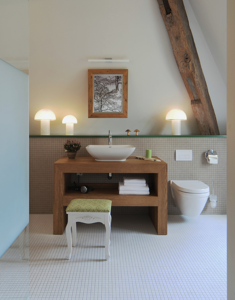 Lantlig inredning av ett stort badrum, med ett fristående handfat, öppna hyllor, skåp i mellenmörkt trä, vit kakel, mosaik, vita väggar, mosaikgolv, en vägghängd toalettstol och träbänkskiva