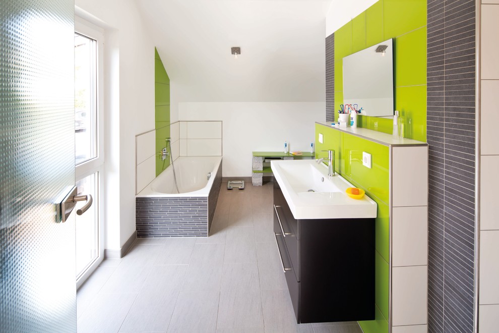 Großes Modernes Badezimmer mit flächenbündigen Schrankfronten, schwarzen Schränken, freistehender Badewanne, grünen Fliesen, Glasfliesen, weißer Wandfarbe, integriertem Waschbecken, grauem Boden und weißer Waschtischplatte in Sonstige