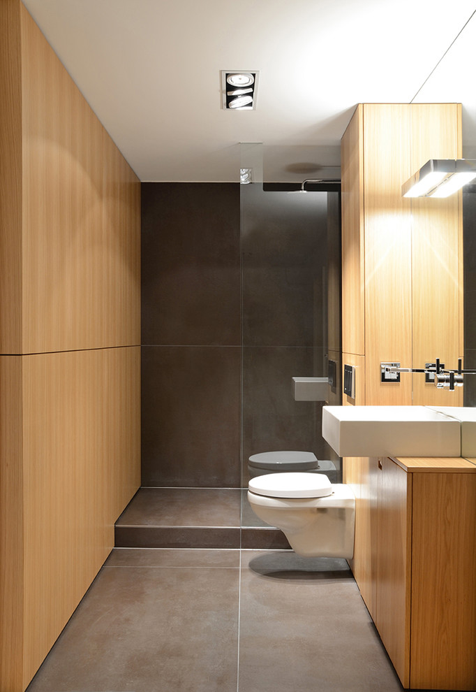 Modern inredning av ett litet badrum med dusch, med släta luckor, skåp i mellenmörkt trä, en dusch i en alkov, en vägghängd toalettstol, grå kakel, ett fristående handfat och träbänkskiva