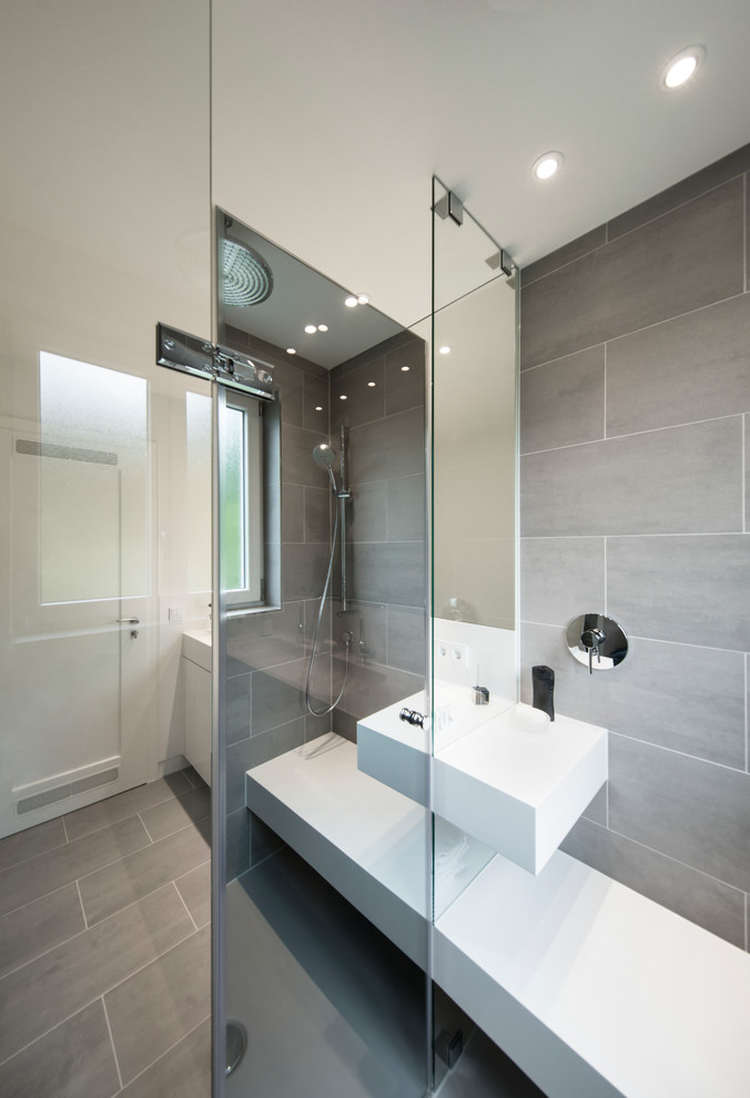 Idéer för ett litet modernt badrum med dusch, med släta luckor, vita skåp, en kantlös dusch, grå kakel, keramikplattor, grå väggar, klinkergolv i keramik, ett avlångt handfat, bänkskiva i akrylsten, grått golv och dusch med gångjärnsdörr