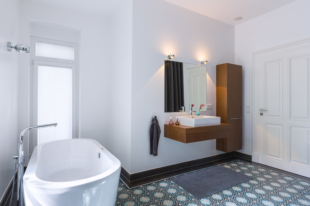 Пример оригинального дизайна: ванная комната среднего размера в скандинавском стиле с настольной раковиной, плоскими фасадами, темными деревянными фасадами, отдельно стоящей ванной, белыми стенами, керамической плиткой, полом из керамической плитки и столешницей из дерева