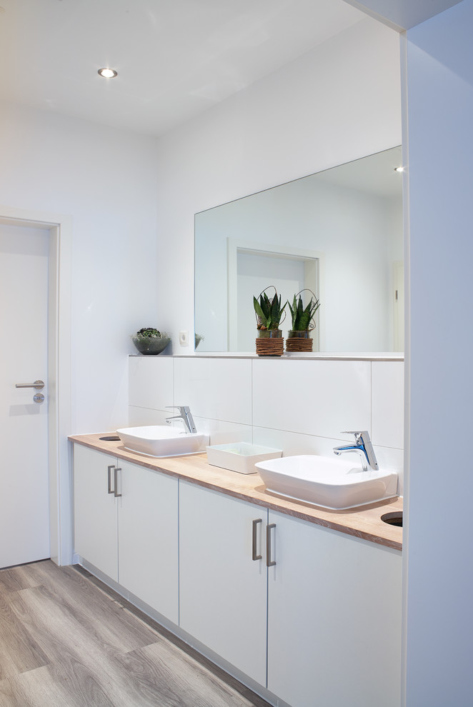 エッセンにある中くらいなコンテンポラリースタイルのおしゃれな浴室 (ベッセル式洗面器、フラットパネル扉のキャビネット、白いキャビネット、白いタイル、白い壁、無垢フローリング、セラミックタイル、木製洗面台) の写真