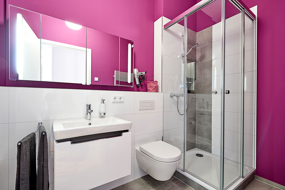 This is an example of a medium sized contemporary family bathroom in Hamburg with flat-panel cabinets, white cabinets, a corner shower, a wall mounted toilet, white tiles, ceramic tiles, pink walls, ceramic flooring, a vessel sink, brown floors, a hinged door and solid surface worktops.