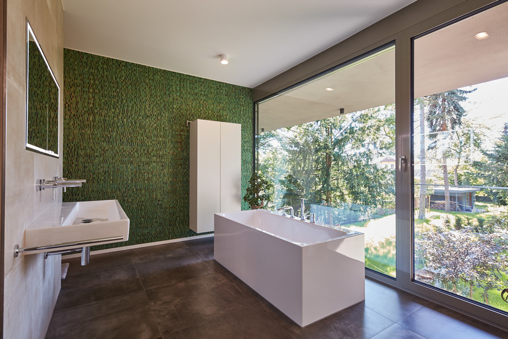 This is an example of a medium sized modern bathroom in Dresden with flat-panel cabinets, white cabinets, a freestanding bath, grey tiles, green tiles, mosaic tiles, beige walls and a wall-mounted sink.