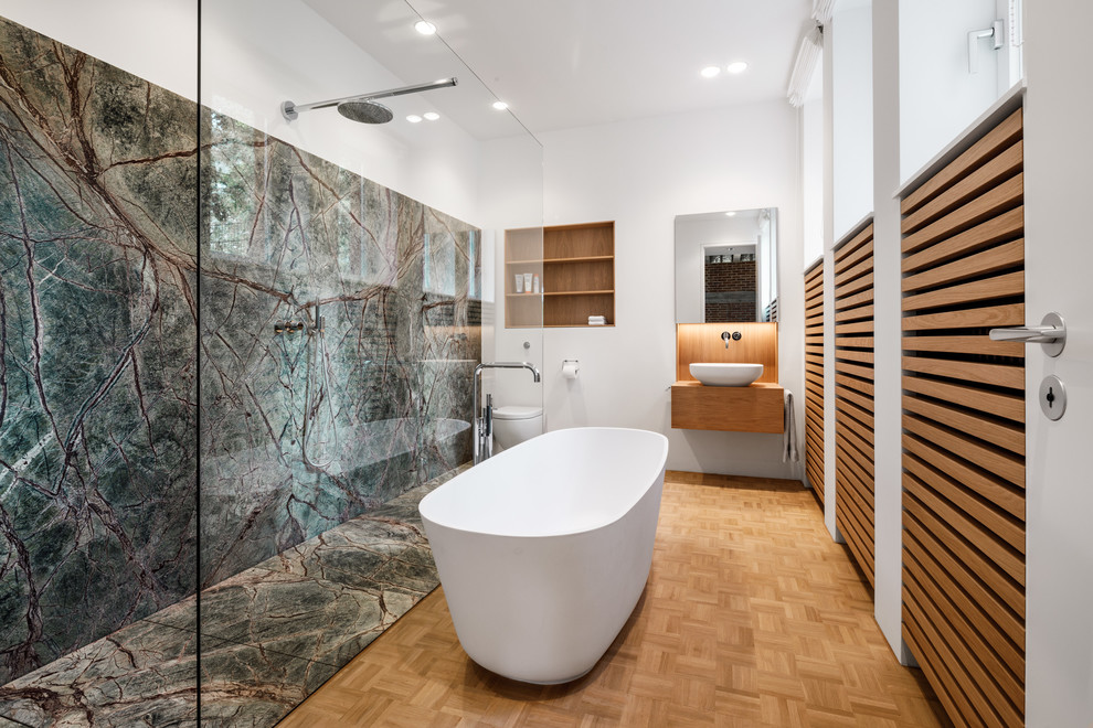 Modernes Duschbad mit Lamellenschränken, hellbraunen Holzschränken, freistehender Badewanne, Nasszelle, grünen Fliesen, Steinplatten, weißer Wandfarbe und braunem Holzboden in Köln