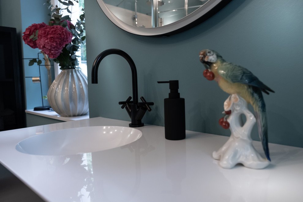 Inredning av ett modernt stort vit vitt badrum, med släta luckor, grå skåp, en toalettstol med separat cisternkåpa, cementgolv, ett nedsänkt handfat, bänkskiva i akrylsten och turkost golv