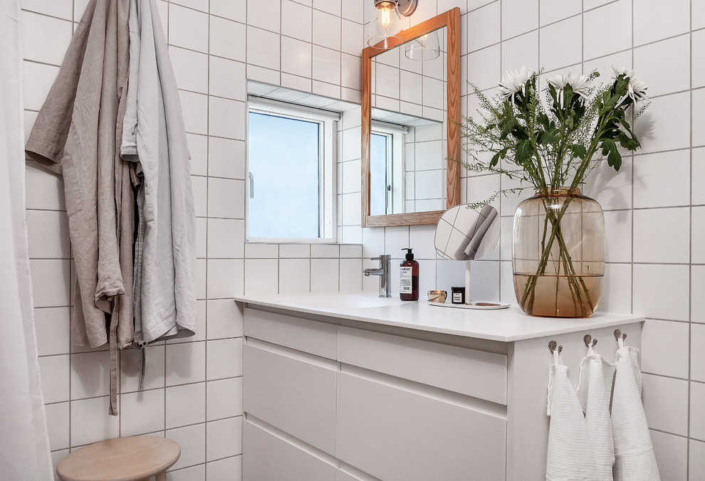 Foto på ett mellanstort nordiskt badrum med dusch, med släta luckor, vita skåp, vit kakel, ett undermonterad handfat, keramikplattor och vita väggar
