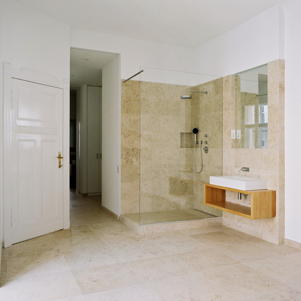Cette image montre une salle de bain beige et blanche design avec un placard sans porte, une douche d'angle, un carrelage beige, un carrelage de pierre, un mur blanc, un sol en travertin, une vasque et un plan de toilette en bois.