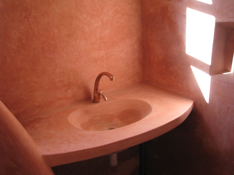 Cette image montre une salle de bain méditerranéenne avec tomettes au sol, un lavabo intégré et un mur rouge.