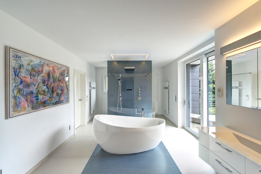 Großes Modernes Badezimmer En Suite mit bodengleicher Dusche, blauen Fliesen, weißer Wandfarbe, flächenbündigen Schrankfronten, weißen Schränken, freistehender Badewanne, integriertem Waschbecken und Mineralwerkstoff-Waschtisch in Leipzig
