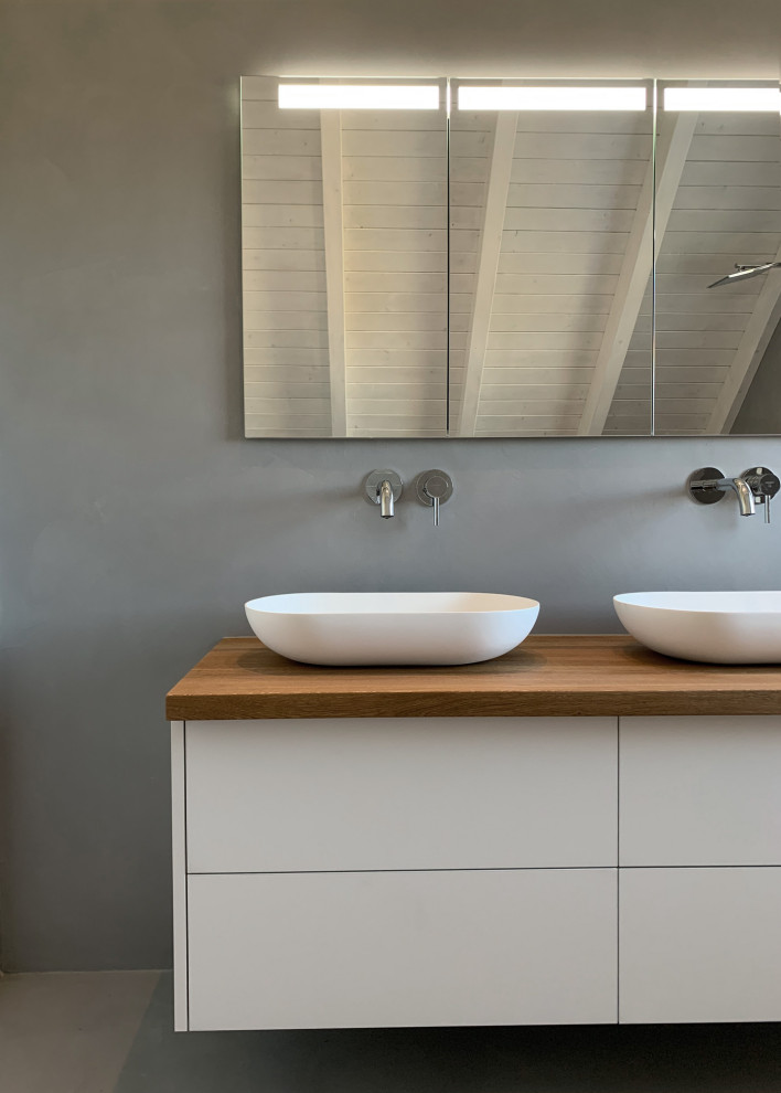 Exempel på ett litet modernt brun brunt badrum med dusch, med släta luckor, vita skåp, en kantlös dusch, en vägghängd toalettstol, grå kakel, marmorkakel, vita väggar, betonggolv, ett fristående handfat, träbänkskiva, grått golv och med dusch som är öppen