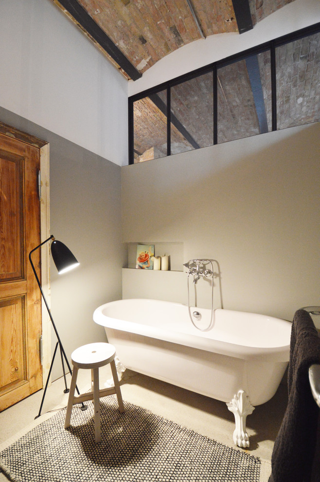Industriell inredning av ett litet badrum, med ett fristående badkar, beige väggar och betonggolv