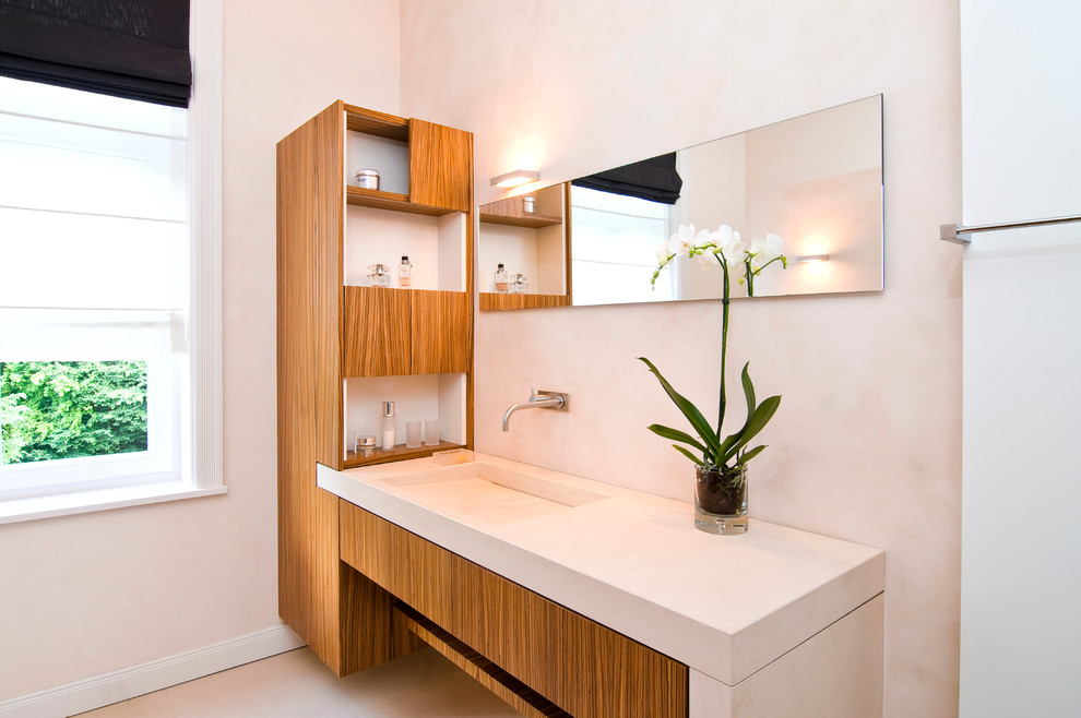 Modern inredning av ett mellanstort badrum med dusch, med ett integrerad handfat, släta luckor, skåp i mellenmörkt trä, bänkskiva i kalksten, en kantlös dusch, en vägghängd toalettstol, stenhäll, beige väggar och kalkstensgolv