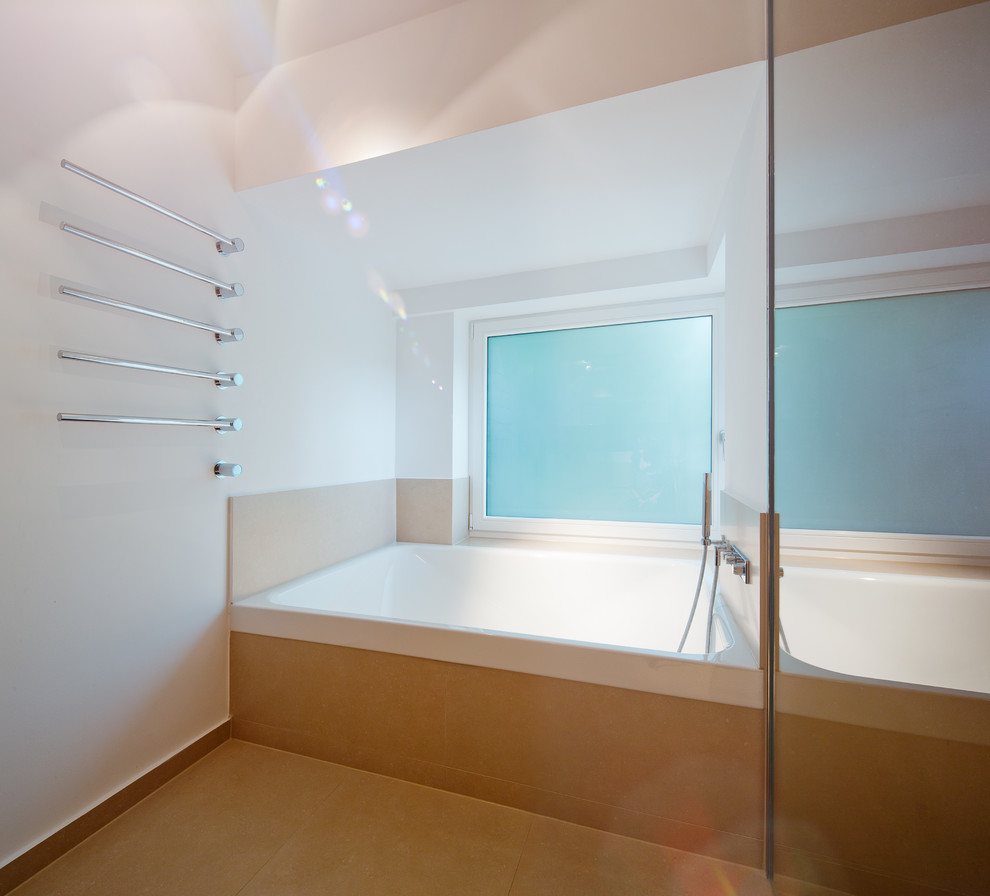 Réalisation d'une salle de bain design avec une baignoire en alcôve, un carrelage beige, un mur blanc et une fenêtre.