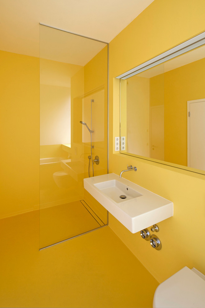 Modelo de cuarto de baño contemporáneo pequeño con lavabo suspendido, ducha abierta, paredes amarillas, sanitario de pared y ducha abierta