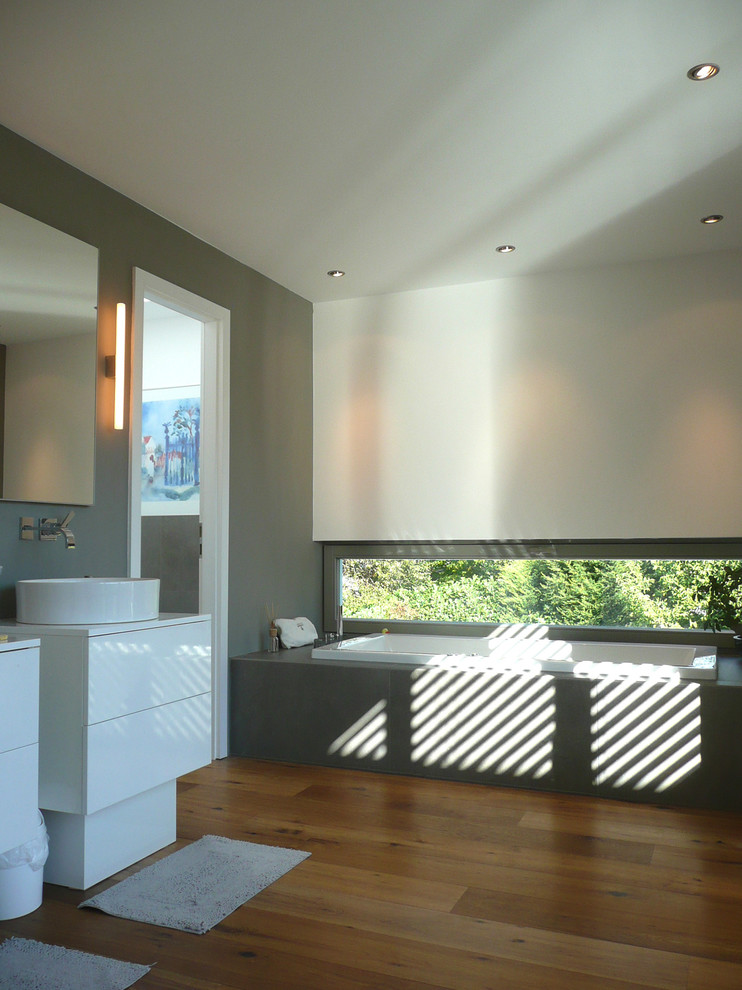 Exempel på ett modernt badrum, med en vägghängd toalettstol, grå väggar, mellanmörkt trägolv, ett fristående handfat, släta luckor, vita skåp och en jacuzzi