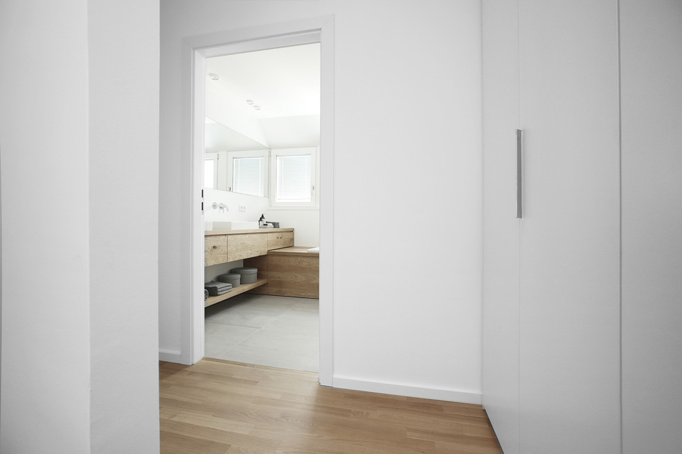 Idée de décoration pour une salle de bain design en bois clair de taille moyenne avec un placard à porte plane, une baignoire posée, un carrelage gris, un mur blanc, une vasque, un plan de toilette en bois et un sol gris.