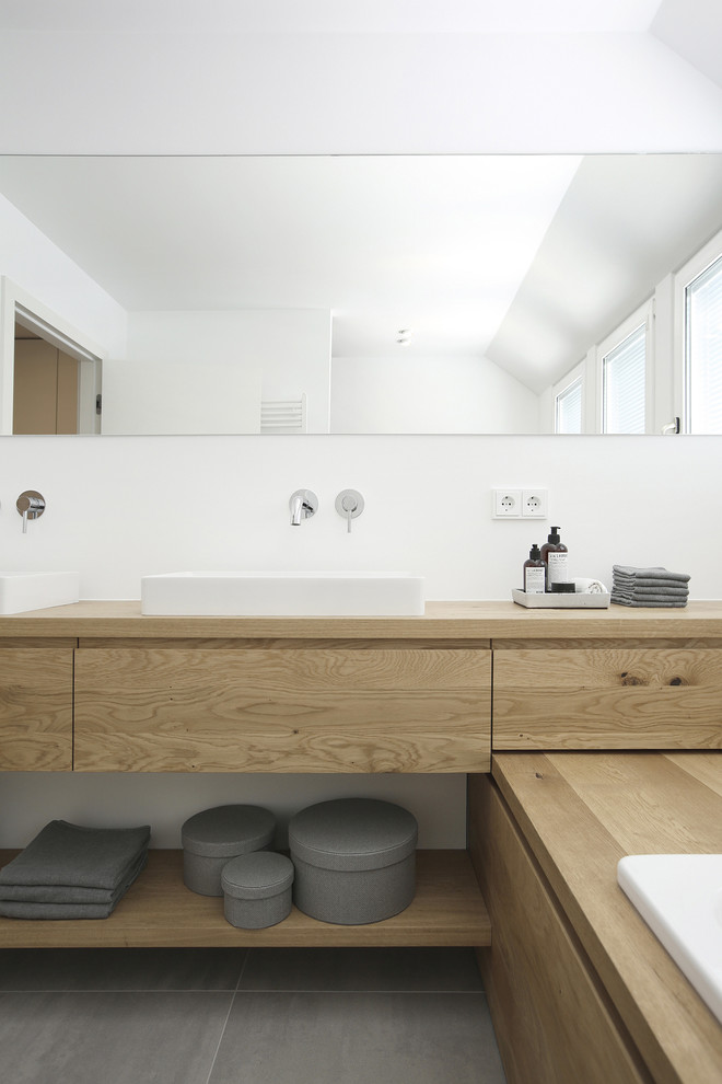 Inspiration för mellanstora moderna badrum, med släta luckor, skåp i ljust trä, ett platsbyggt badkar, grå kakel, vita väggar, ett fristående handfat, träbänkskiva och grått golv