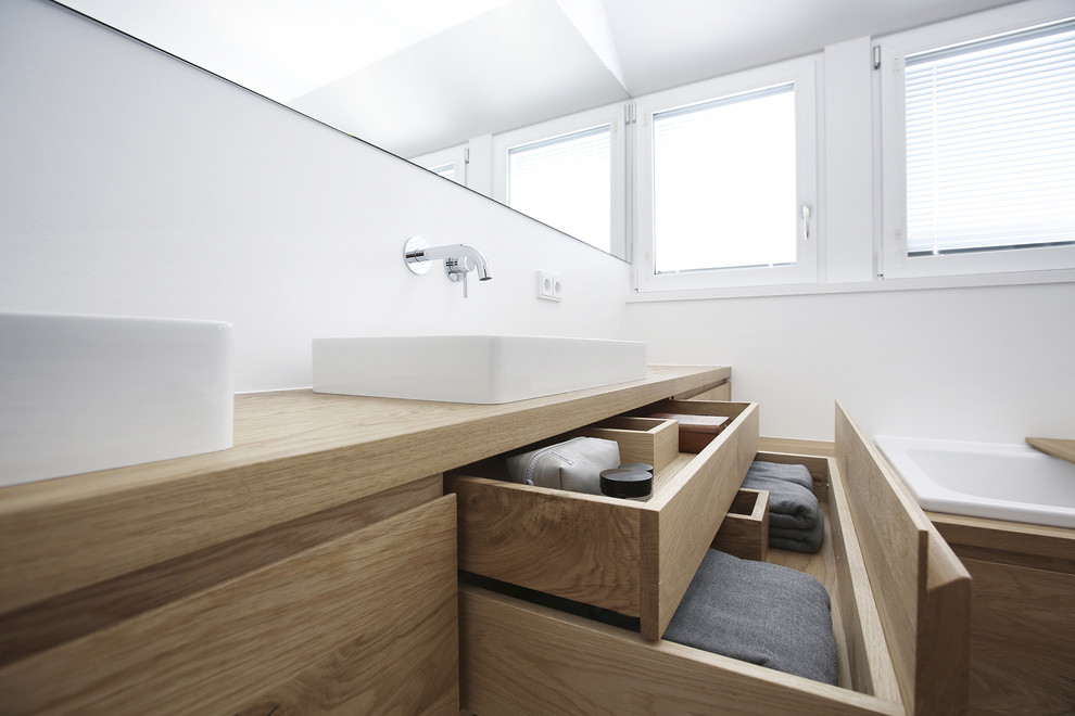 Пример оригинального дизайна: ванная комната среднего размера в современном стиле с плоскими фасадами, светлыми деревянными фасадами, накладной ванной, серой плиткой, белыми стенами, настольной раковиной, столешницей из дерева и серым полом