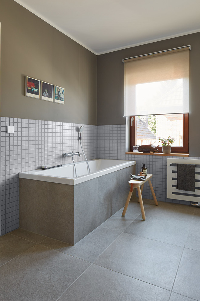 Foto på ett mellanstort funkis badrum, med släta luckor, ett platsbyggt badkar, en vägghängd toalettstol, grå kakel, keramikplattor, grå väggar, klinkergolv i keramik, ett konsol handfat och träbänkskiva