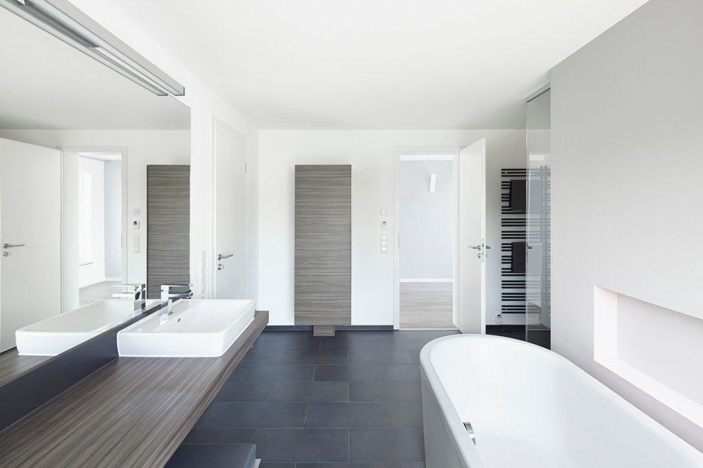 Свежая идея для дизайна: большая ванная комната в стиле модернизм с настольной раковиной, плоскими фасадами, темными деревянными фасадами, столешницей из дерева, отдельно стоящей ванной, черной плиткой, белыми стенами и душем без бортиков - отличное фото интерьера