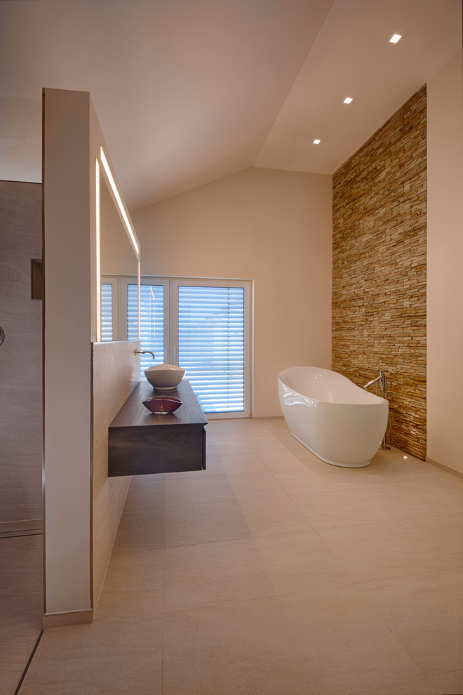 Idée de décoration pour une grande douche en alcôve design en bois foncé avec une vasque, un placard à porte plane, un plan de toilette en bois, une baignoire indépendante, un carrelage beige, un mur blanc, un plan de toilette marron et un mur en pierre.
