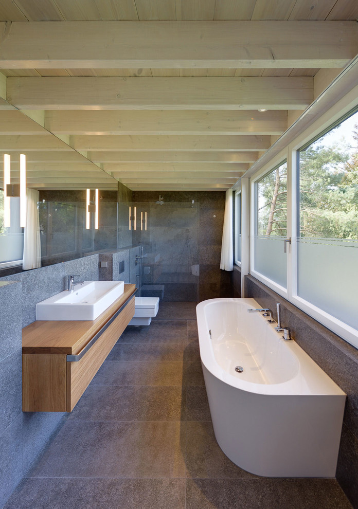 Ispirazione per una stanza da bagno contemporanea di medie dimensioni con ante lisce, ante in legno scuro, WC sospeso, piastrelle grigie, lavabo a bacinella e top in legno