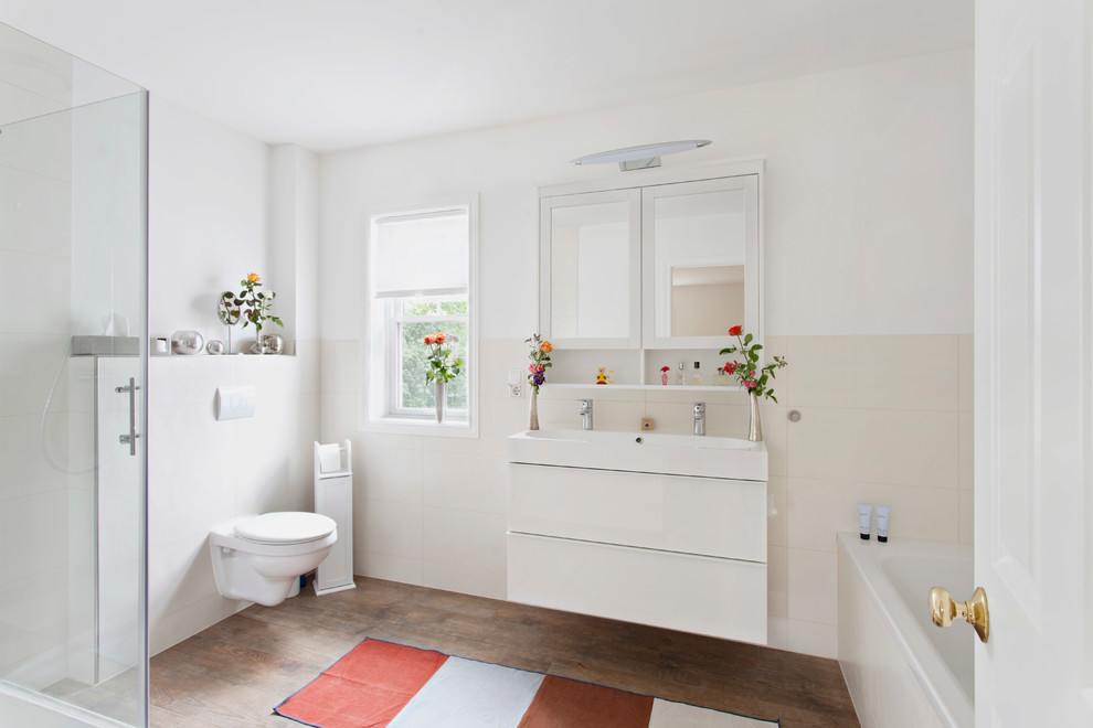 Foto di una stanza da bagno minimal di medie dimensioni con ante lisce, ante bianche, WC sospeso, piastrelle beige, pareti bianche, pavimento in legno massello medio, vasca da incasso, piastrelle in ceramica e lavabo rettangolare