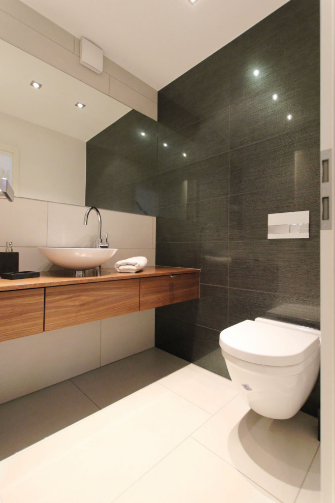 Foto på ett stort funkis brun badrum med dusch, med släta luckor, skåp i mellenmörkt trä, en vägghängd toalettstol, grå kakel, ett fristående handfat, träbänkskiva och beiget golv