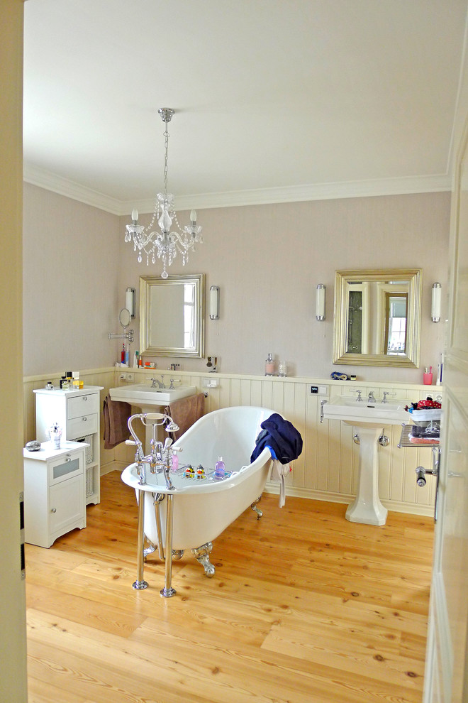 Ejemplo de cuarto de baño campestre de tamaño medio con bañera con patas, paredes beige, suelo de madera clara y lavabo con pedestal