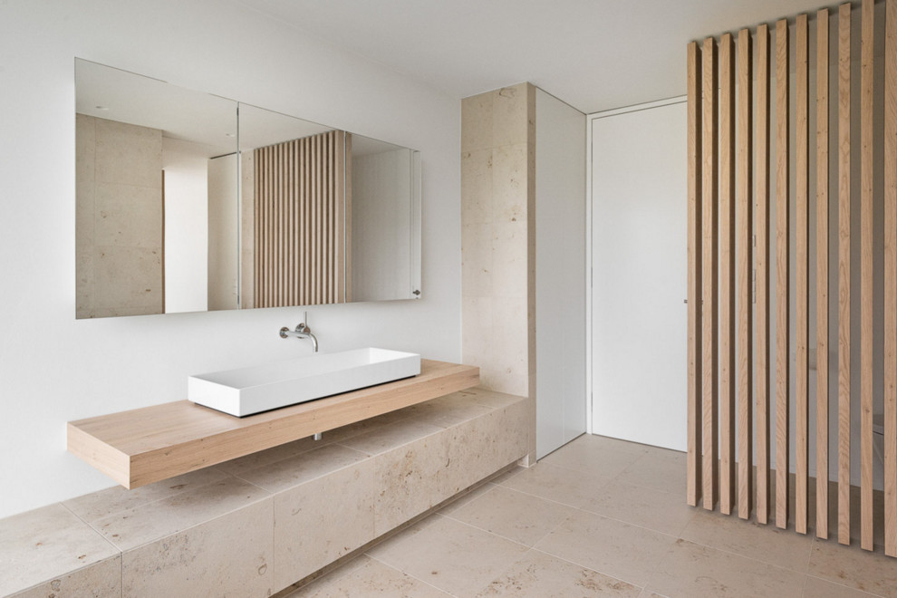 Large trendy beige tile and stone slab limestone floor bathroom photo in Nuremberg with white walls, a vessel sink, wood countertops and beige countertops