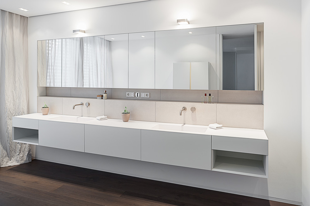 Modernes Badezimmer mit flächenbündigen Schrankfronten, weißen Schränken, Keramikfliesen, weißer Wandfarbe, dunklem Holzboden und integriertem Waschbecken in Köln