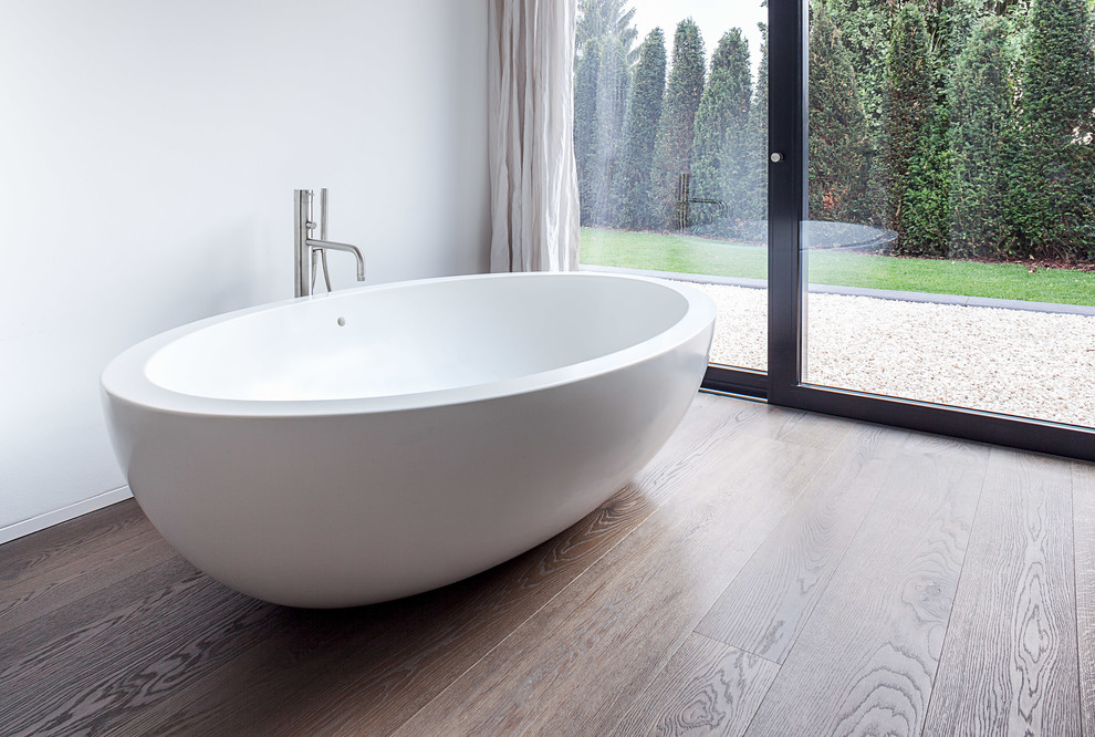 Inspiration pour une salle de bain design avec une baignoire indépendante, parquet foncé et un mur blanc.