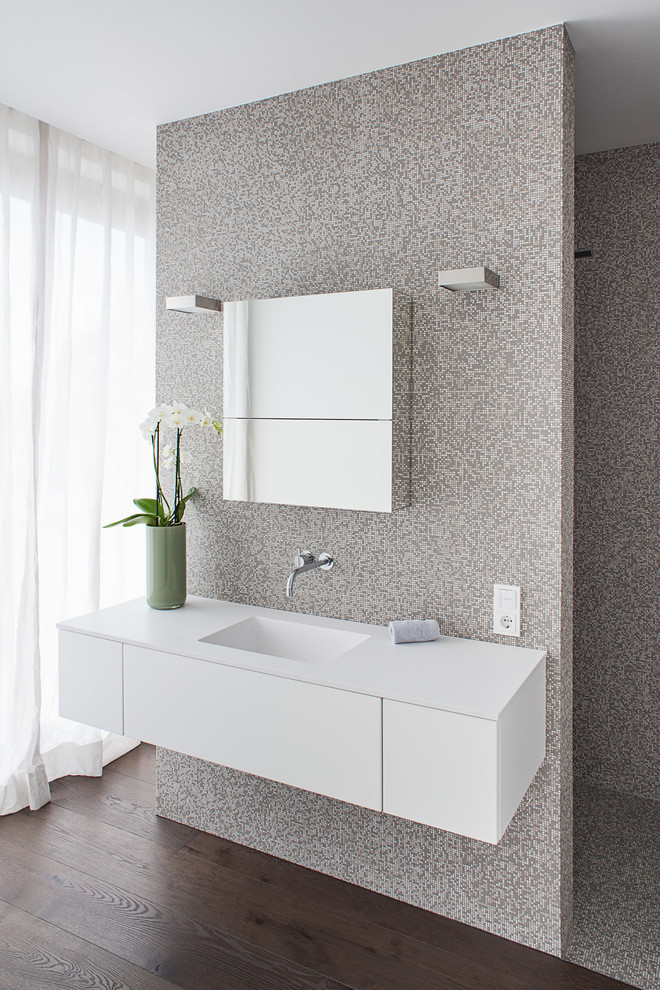 Badezimmer mit integriertem Waschbecken, flächenbündigen Schrankfronten, weißen Schränken, Duschnische, grauen Fliesen, Mosaikfliesen, beiger Wandfarbe und dunklem Holzboden in Köln