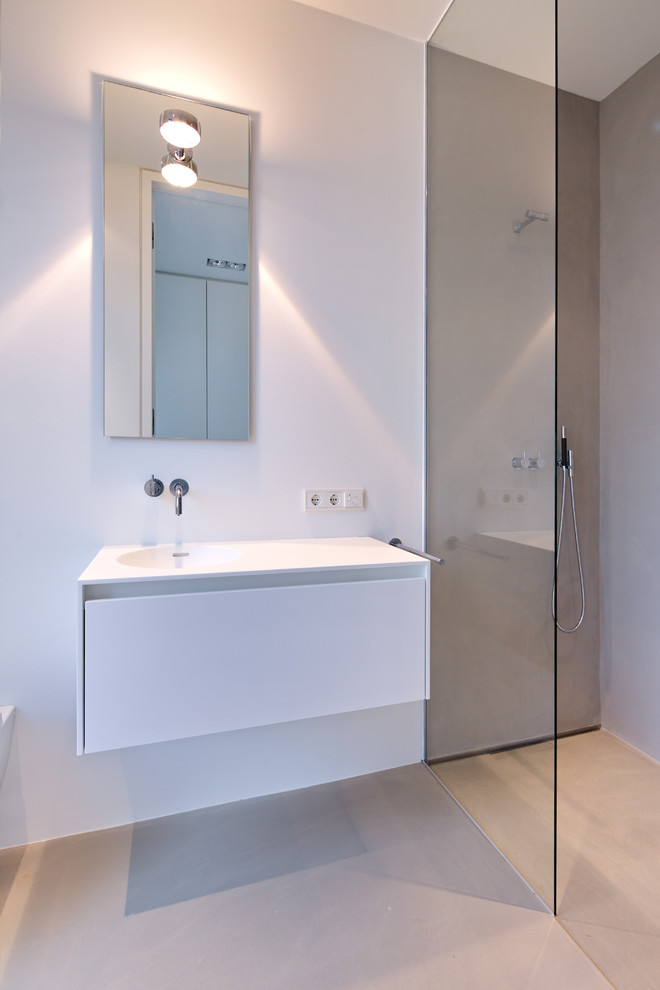 Foto på ett mellanstort funkis badrum med dusch, med släta luckor, vita skåp, en kantlös dusch, vita väggar, bänkskiva i akrylsten, grått golv, med dusch som är öppen, en vägghängd toalettstol, betonggolv och ett integrerad handfat