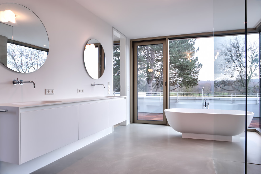 Inredning av ett modernt mycket stort en-suite badrum, med släta luckor, vita skåp, ett fristående badkar, en kantlös dusch, vita väggar, betonggolv, ett integrerad handfat, bänkskiva i akrylsten, grått golv och med dusch som är öppen