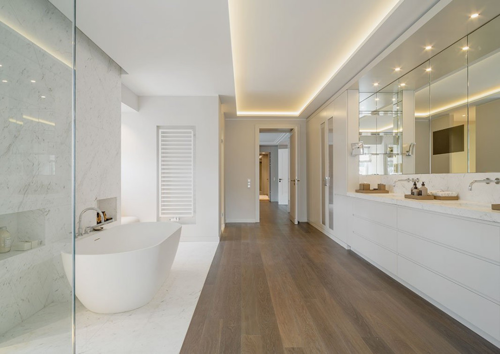 Foto på ett mycket stort funkis grå badrum med dusch, med släta luckor, grå skåp, ett fristående badkar, en öppen dusch, grå kakel, vit kakel, grå väggar, ett undermonterad handfat och brunt golv
