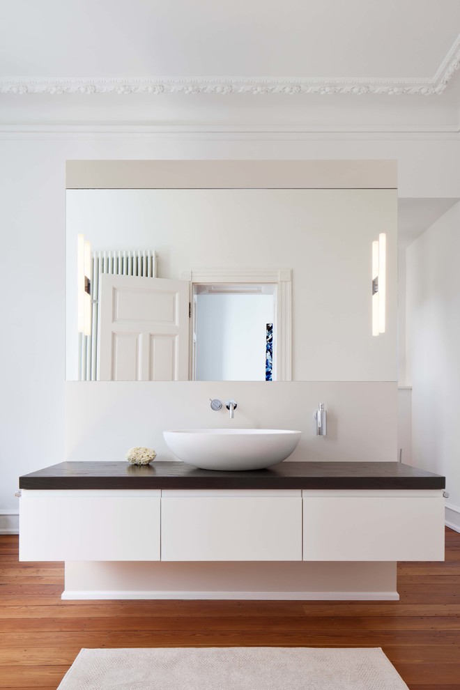 На фото: главная ванная комната среднего размера в современном стиле с плоскими фасадами, белыми фасадами, белыми стенами, паркетным полом среднего тона, настольной раковиной и столешницей из дерева с