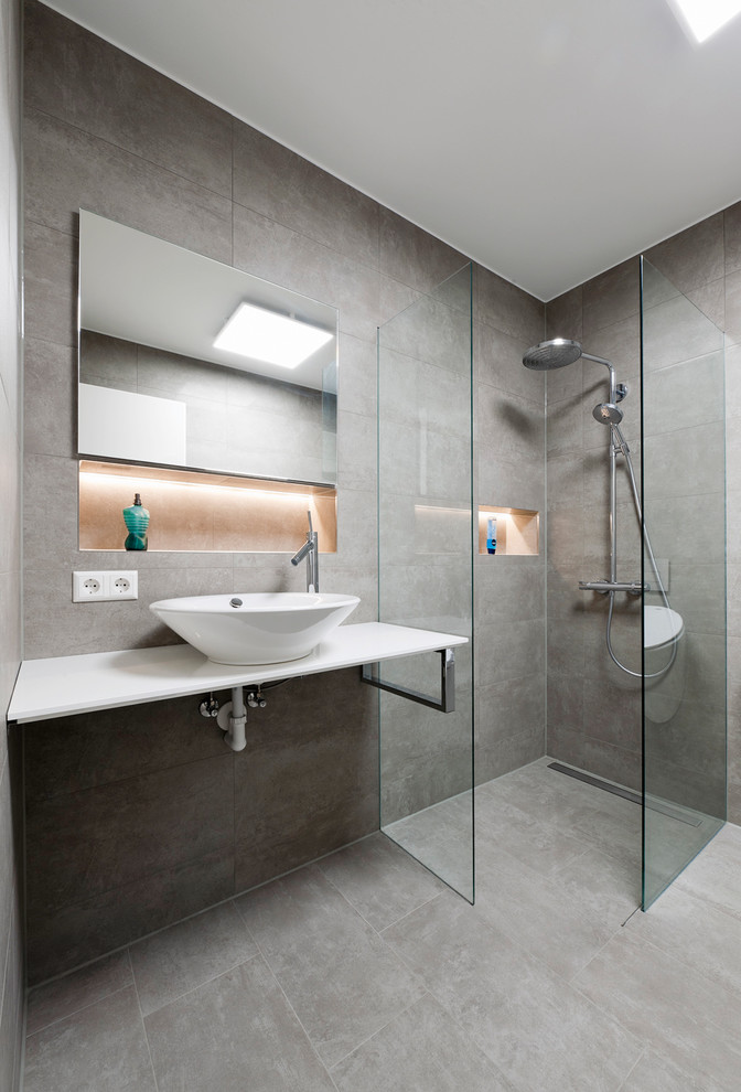 Idéer för att renovera ett mellanstort funkis badrum med dusch, med släta luckor, vita skåp, en kantlös dusch, grå kakel, stenhäll, grå väggar, ett fristående handfat och med dusch som är öppen